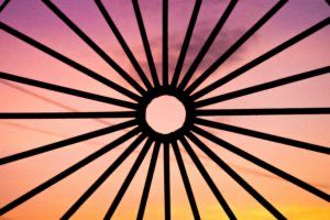 sunset seen through iron bars in the foreground all pointing in towards a circle in the centre made of iron, so that the iron structure silhouette looks like a sun against the backdrop of the sunset